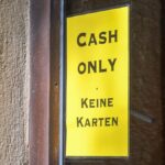 Gelbes Schild an einer Tür mit der Aufschrift „Cash only“ und „Keine Karten“.