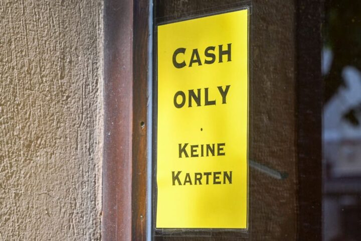 Gelbes Schild an einer Tür mit der Aufschrift „Cash only“ und „Keine Karten“.