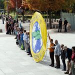 Menschen stehen in einer langen Kette auf einem Platz, vorne ein großes gelbes Klimaschutz-Banner.