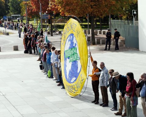 Menschen stehen in einer langen Kette auf einem Platz, vorne ein großes gelbes Klimaschutz-Banner.