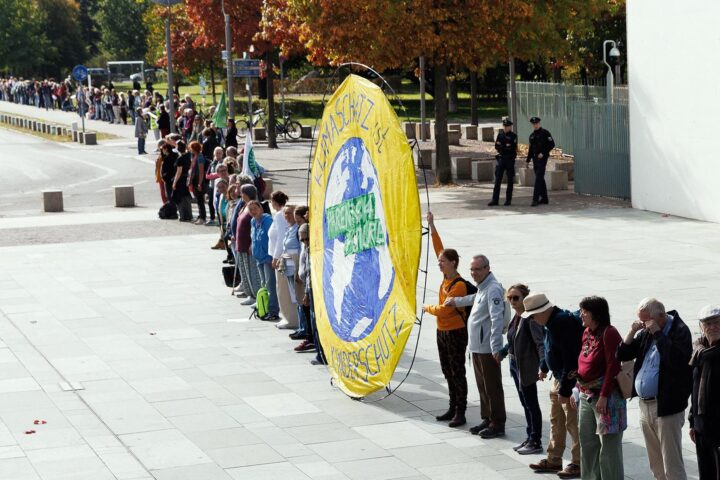 Menschen stehen in einer langen Kette auf einem Platz, vorne ein großes gelbes Klimaschutz-Banner.