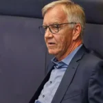 Dietmar Bartsch steht mit Brille und dunkelblauem Sakko vor einem grauen Hintergrund.