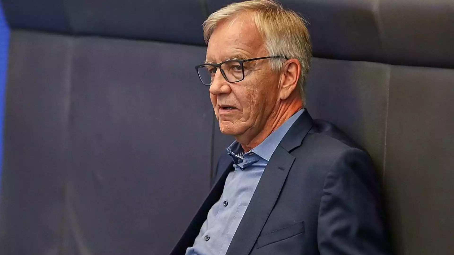 Bartsch distanziert sich von Köktürks Instagram-Video und kündigt Beratung an 1 Dietmar Bartsch steht mit Brille und dunkelblauem Sakko vor einem grauen Hintergrund.