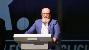 Bärtiger Mann mit Brille spricht an einem Rednerpult auf einer Bühne.