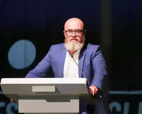 Bärtiger Mann mit Brille spricht an einem Rednerpult auf einer Bühne.