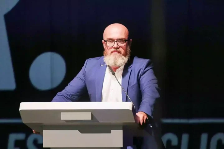 Bärtiger Mann mit Brille spricht an einem Rednerpult auf einer Bühne.