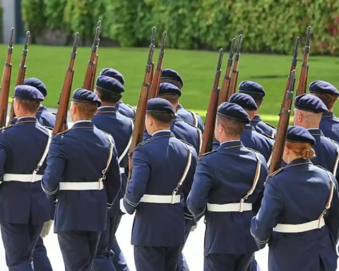 Mehrere uniformierte Soldaten marschieren mit Gewehren bei einer militärischen Formation.