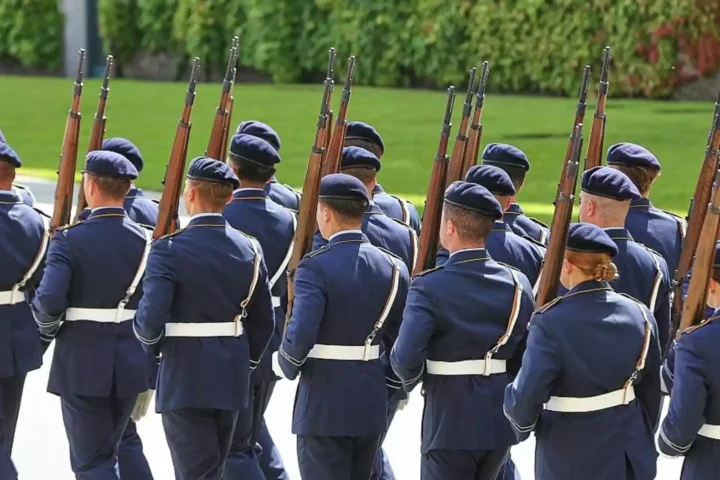Mehrere uniformierte Soldaten marschieren mit Gewehren bei einer militärischen Formation.