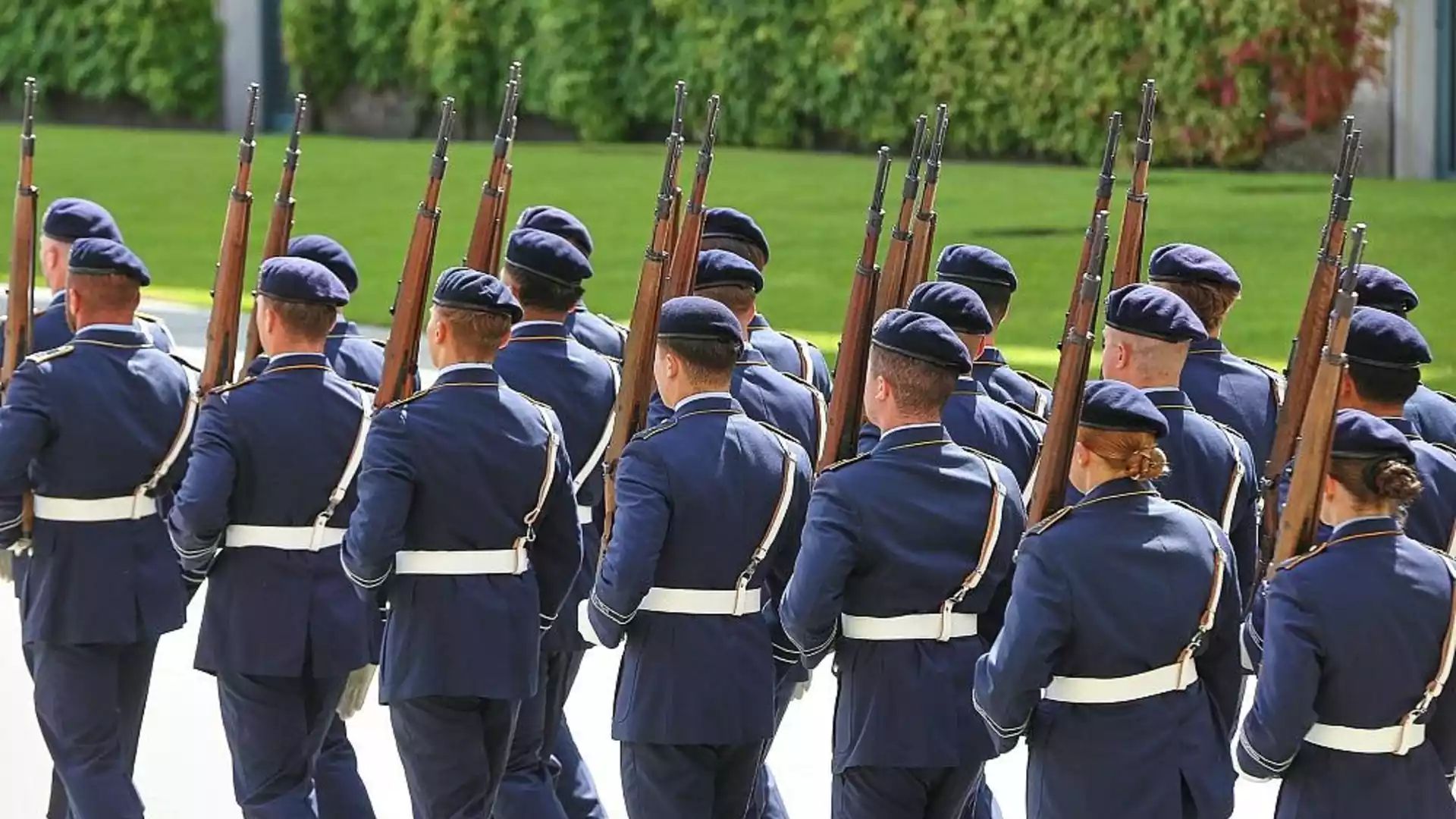 Mehrere uniformierte Soldaten marschieren mit Gewehren bei einer militärischen Formation.