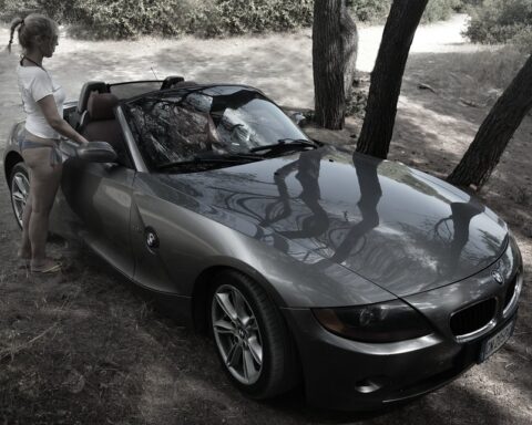 Eine Frau steht neben einem BMW-Cabrio im Freien zwischen Bäumen.