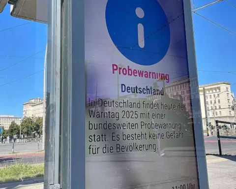 German public warning notice at a city street stop with a blue information symbol and the word “Probewarnung”.