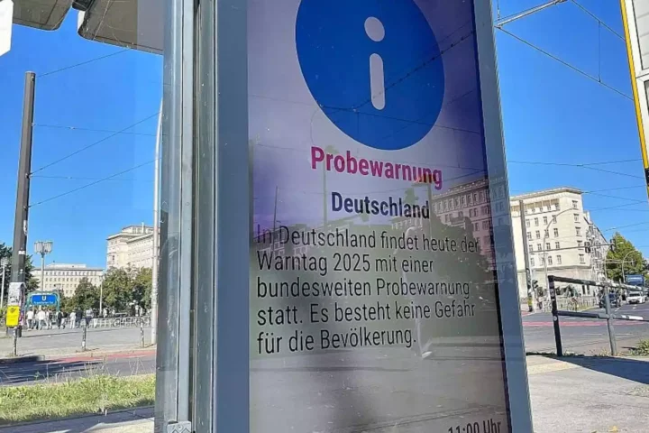 German public warning notice at a city street stop with a blue information symbol and the word “Probewarnung”.