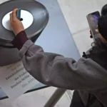 Eine Person fotografiert eine Abstimmungsanzeige an einer Installation mit einem Smartphone.
