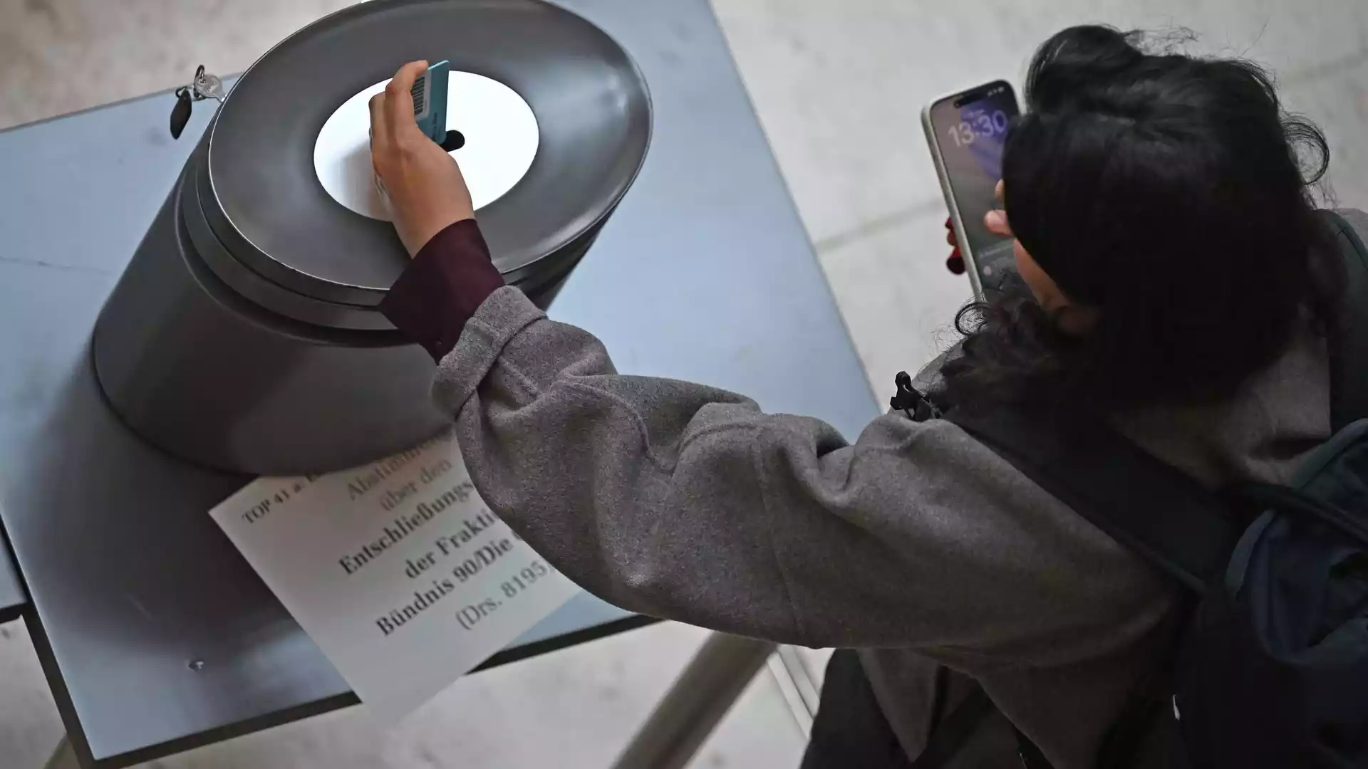 Eine Person fotografiert eine Abstimmungsanzeige an einer Installation mit einem Smartphone.