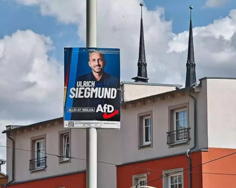 AfD-Wahlplakat mit dem Porträt von Ulrich Siegmund an einer Straße vor Gebäuden und Kirchturmspitzen.