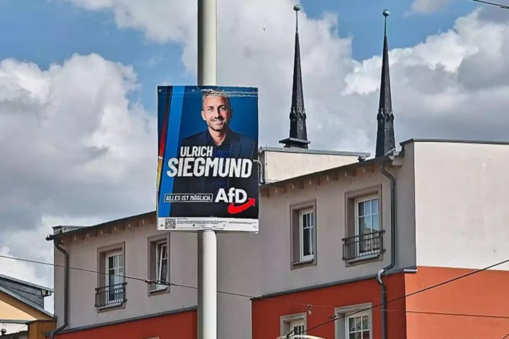 AfD-Wahlplakat mit dem Porträt von Ulrich Siegmund an einer Straße vor Gebäuden und Kirchturmspitzen.