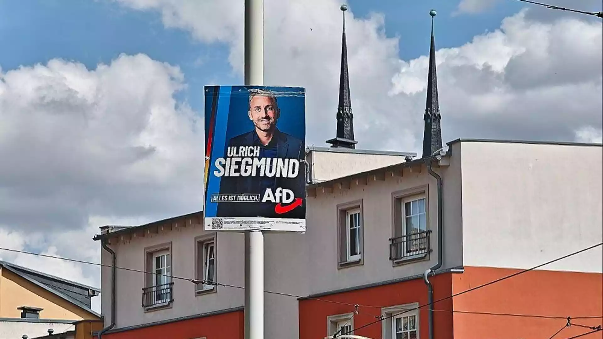AfD-Wahlplakat mit dem Porträt von Ulrich Siegmund an einer Straße vor Gebäuden und Kirchturmspitzen.
