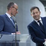 Zwei Politiker stehen an transparenten Redepulten in einem modernen Innenraum.