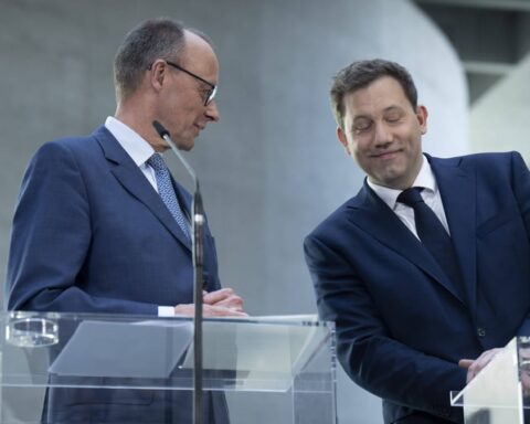 Zwei Politiker stehen an transparenten Redepulten in einem modernen Innenraum.