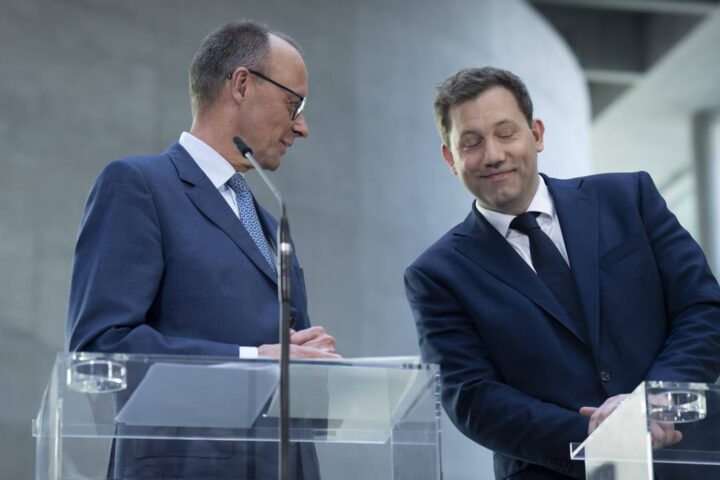 Zwei Politiker stehen an transparenten Redepulten in einem modernen Innenraum.