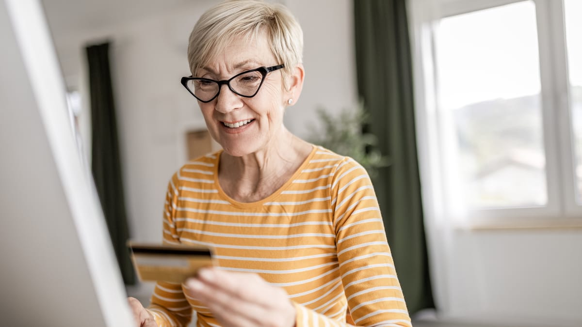 Deutschland plant neues Altersvorsorgedepot mit staatlicher Förderung ab 2027 1 Ältere Frau mit Brille hält eine Kreditkarte vor einem Computerbildschirm.