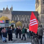 Menschen demonstrieren vor dem Magdeburger Dom, im Vordergrund eine rote Fahne.
