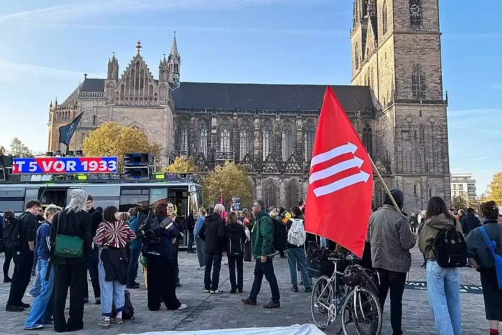 Menschen demonstrieren vor dem Magdeburger Dom, im Vordergrund eine rote Fahne.