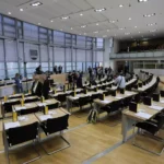 Blick in den Plenarsaal des Landtags von Sachsen-Anhalt mit vorbereiteten Sitzreihen und einigen Menschen im Saal.