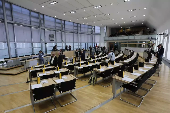 Blick in den Plenarsaal des Landtags von Sachsen-Anhalt mit vorbereiteten Sitzreihen und einigen Menschen im Saal.