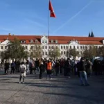 Menschen versammeln sich vor einem historischen Regierungsgebäude in Magdeburg mit roter Fahne auf dem Dach.