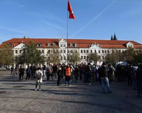 Menschen versammeln sich vor einem historischen Regierungsgebäude in Magdeburg mit roter Fahne auf dem Dach.