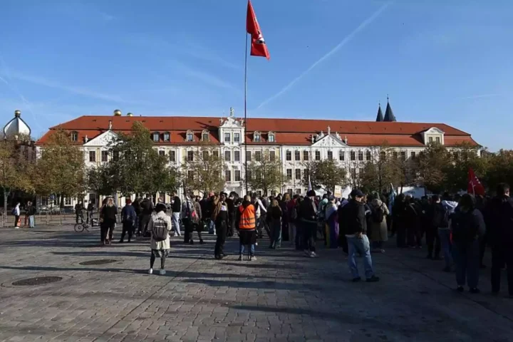 Menschen versammeln sich vor einem historischen Regierungsgebäude in Magdeburg mit roter Fahne auf dem Dach.