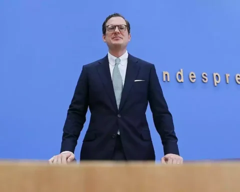 Moritz Hennemann steht vor blauem Hintergrund am Rednerpult bei einer Pressekonferenz.