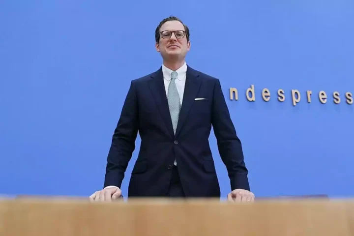 Moritz Hennemann steht vor blauem Hintergrund am Rednerpult bei einer Pressekonferenz.
