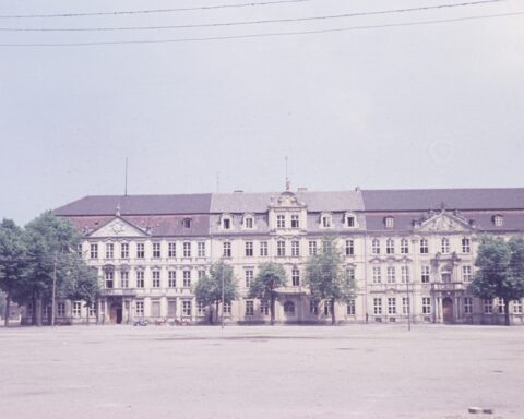Historisches Parlaments- oder Regierungsgebäude mit langer Fassade und Bäumen davor.