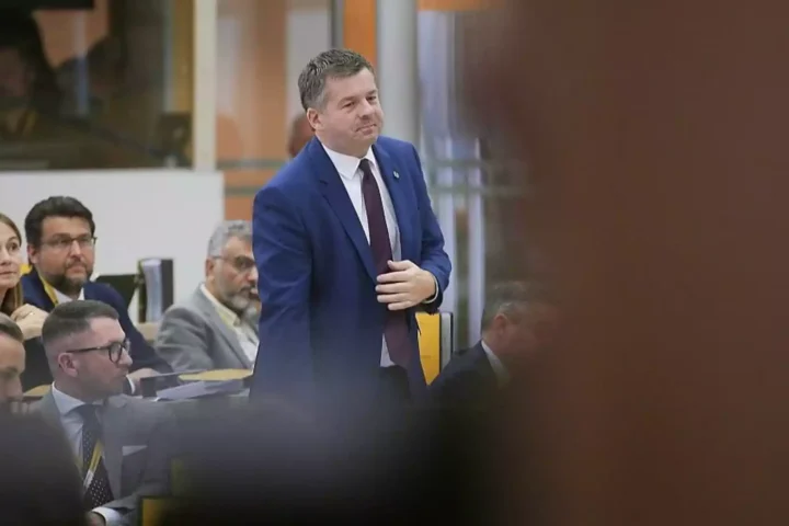 Tobias Rausch steht in einem Plenarsaal und spricht vor mehreren Abgeordneten.