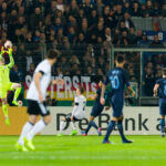 Torwart in neongelbem Trikot fängt einen Ball im Strafraum vor Zuschauern im Stadion.