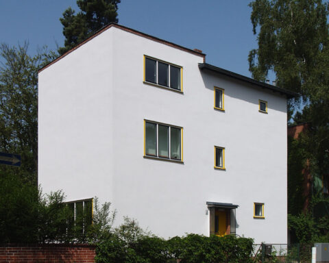 Mehrstöckiges Wohnhaus mit weißer Fassade an einer ruhigen Straße.