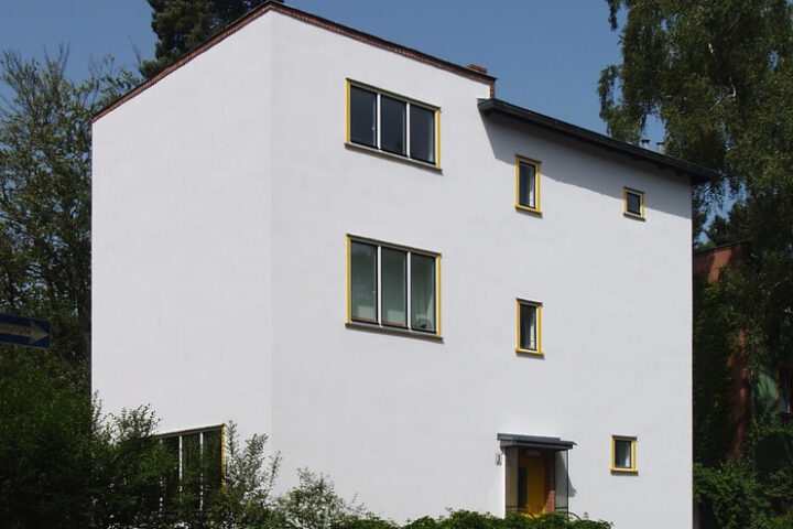 Mehrstöckiges Wohnhaus mit weißer Fassade an einer ruhigen Straße.