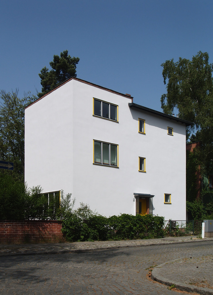 Mehrstöckiges Wohnhaus mit weißer Fassade an einer ruhigen Straße.