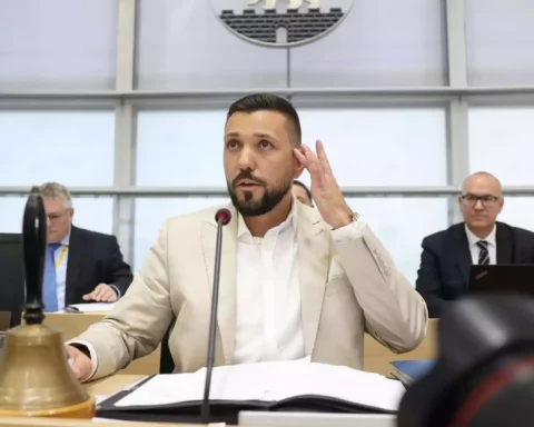 Ein Mann im hellen Anzug spricht am Mikrofon während einer Sitzung im Parlament.