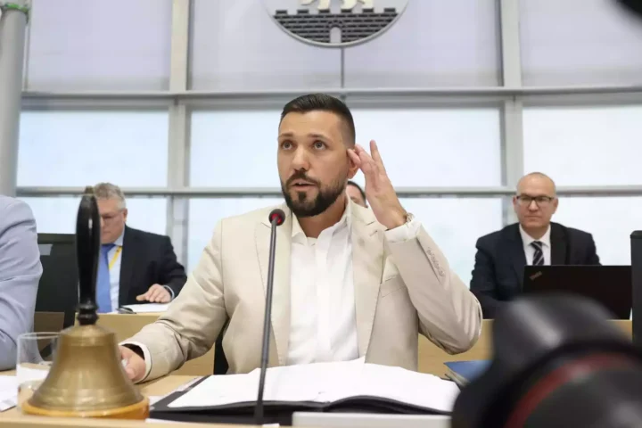 Ein Mann im hellen Anzug spricht am Mikrofon während einer Sitzung im Parlament.