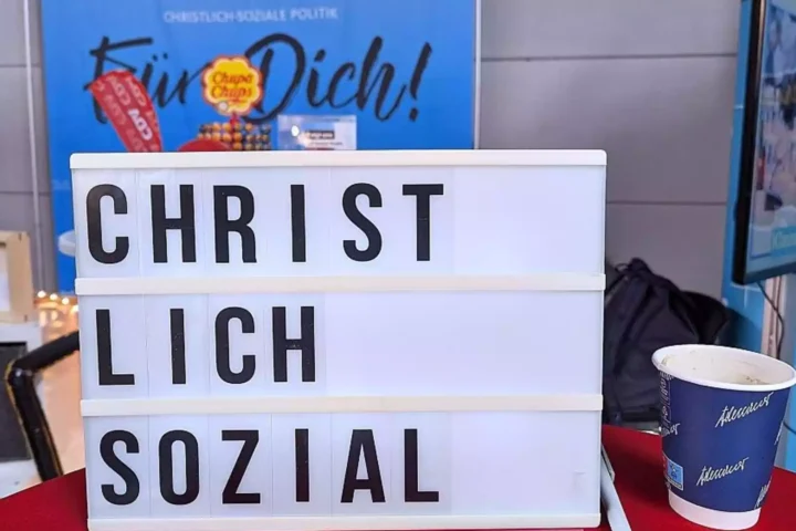 Leuchttafel mit der Aufschrift „CHRIST LICH SOZIAL“ vor einem politischen Stand.