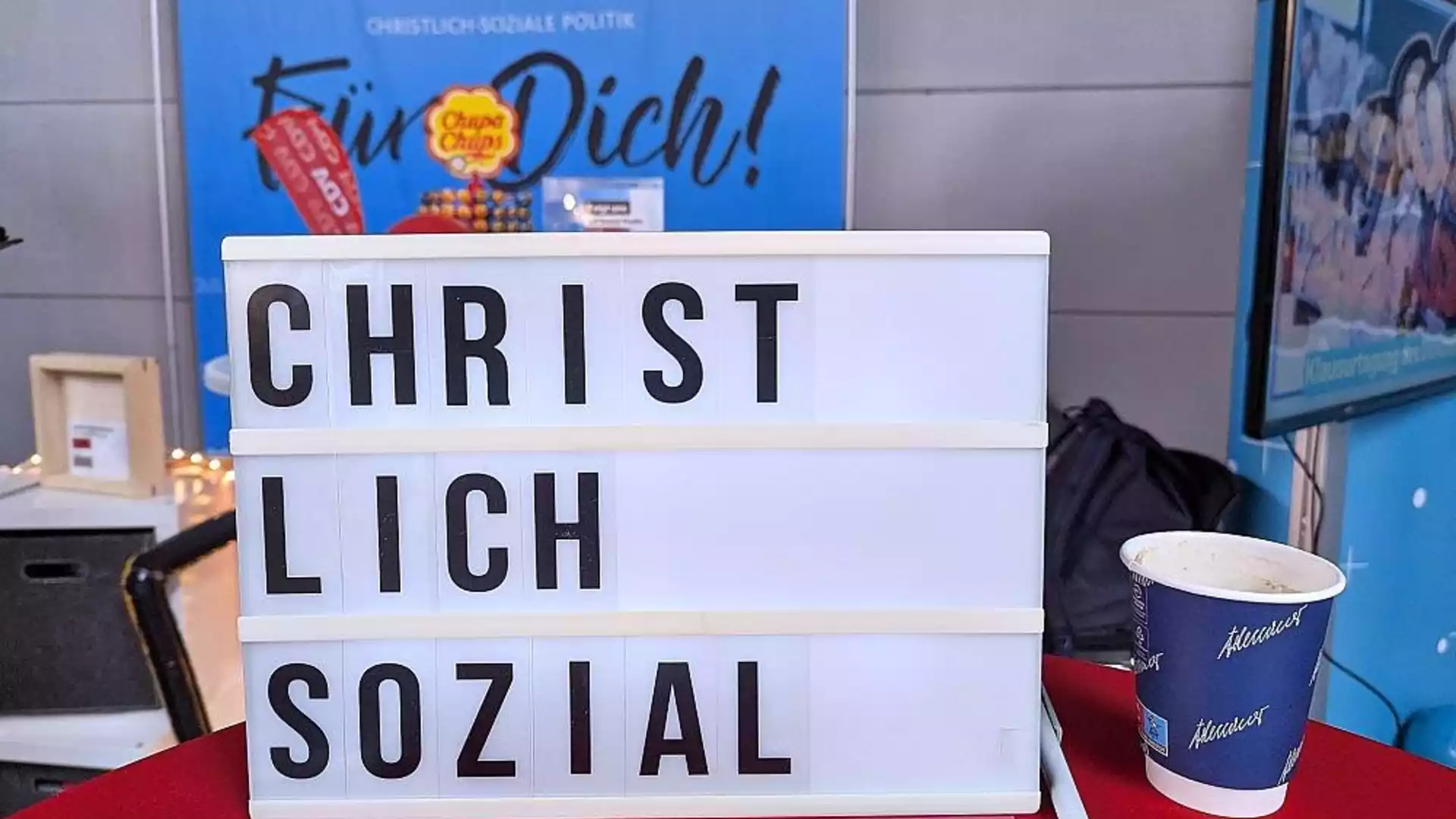 Leuchttafel mit der Aufschrift „CHRIST LICH SOZIAL“ vor einem politischen Stand.