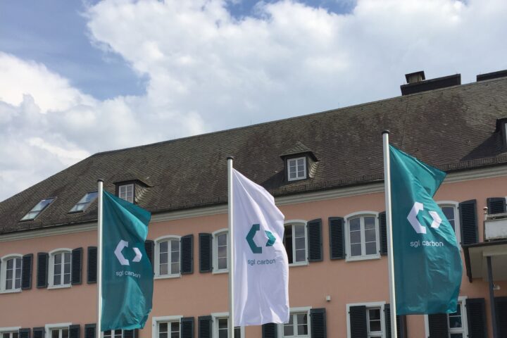 SGL-Carbon-Fahnen vor einem Gebäude mit rosafarbener Fassade und dunklem Dach.