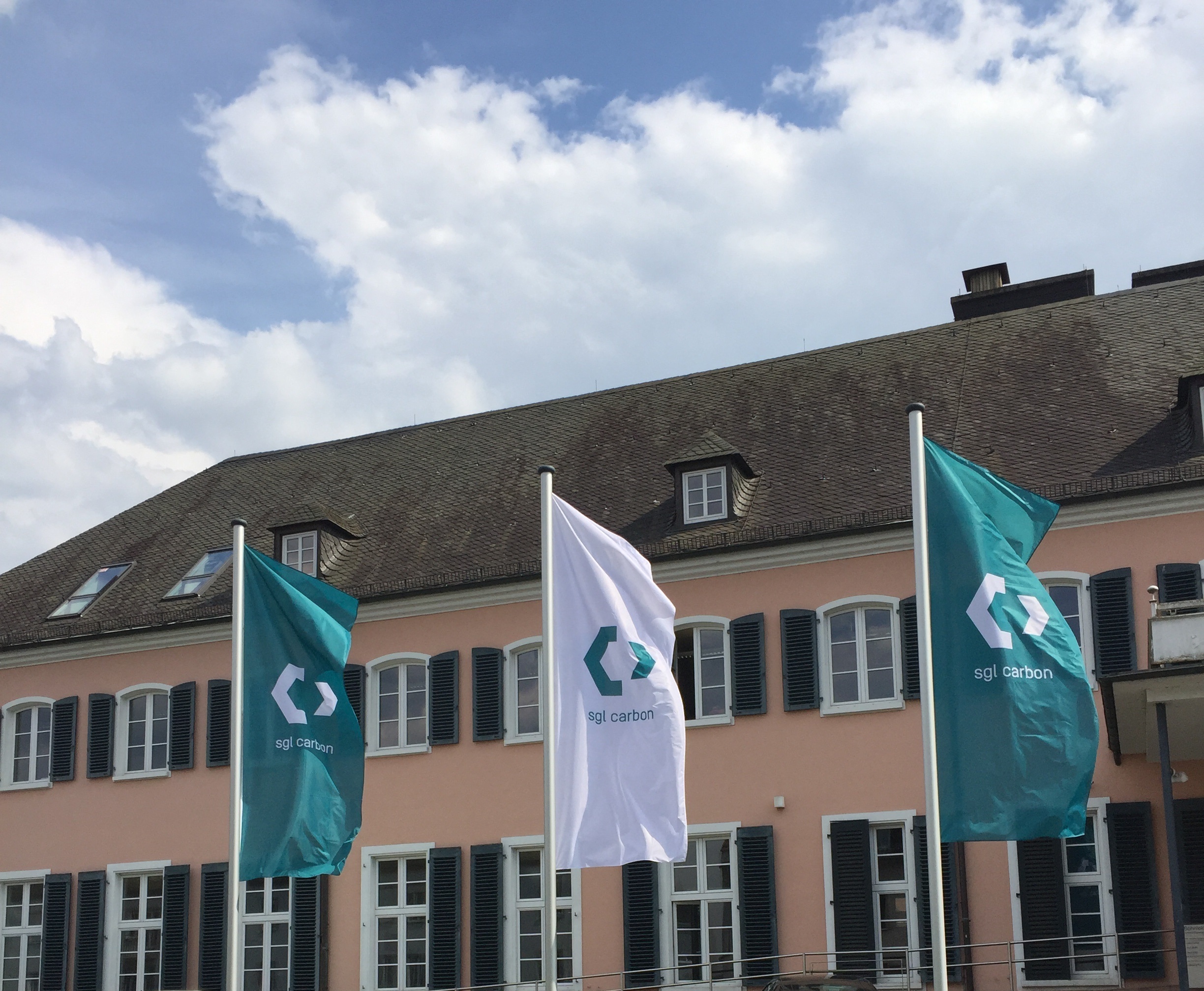 SGL-Carbon-Fahnen vor einem Gebäude mit rosafarbener Fassade und dunklem Dach.