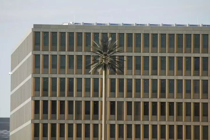 Außenansicht eines modernen Bürogebäudes mit vielen schmalen Fenstern und einer hohen Mastskulptur vor der Fassade.