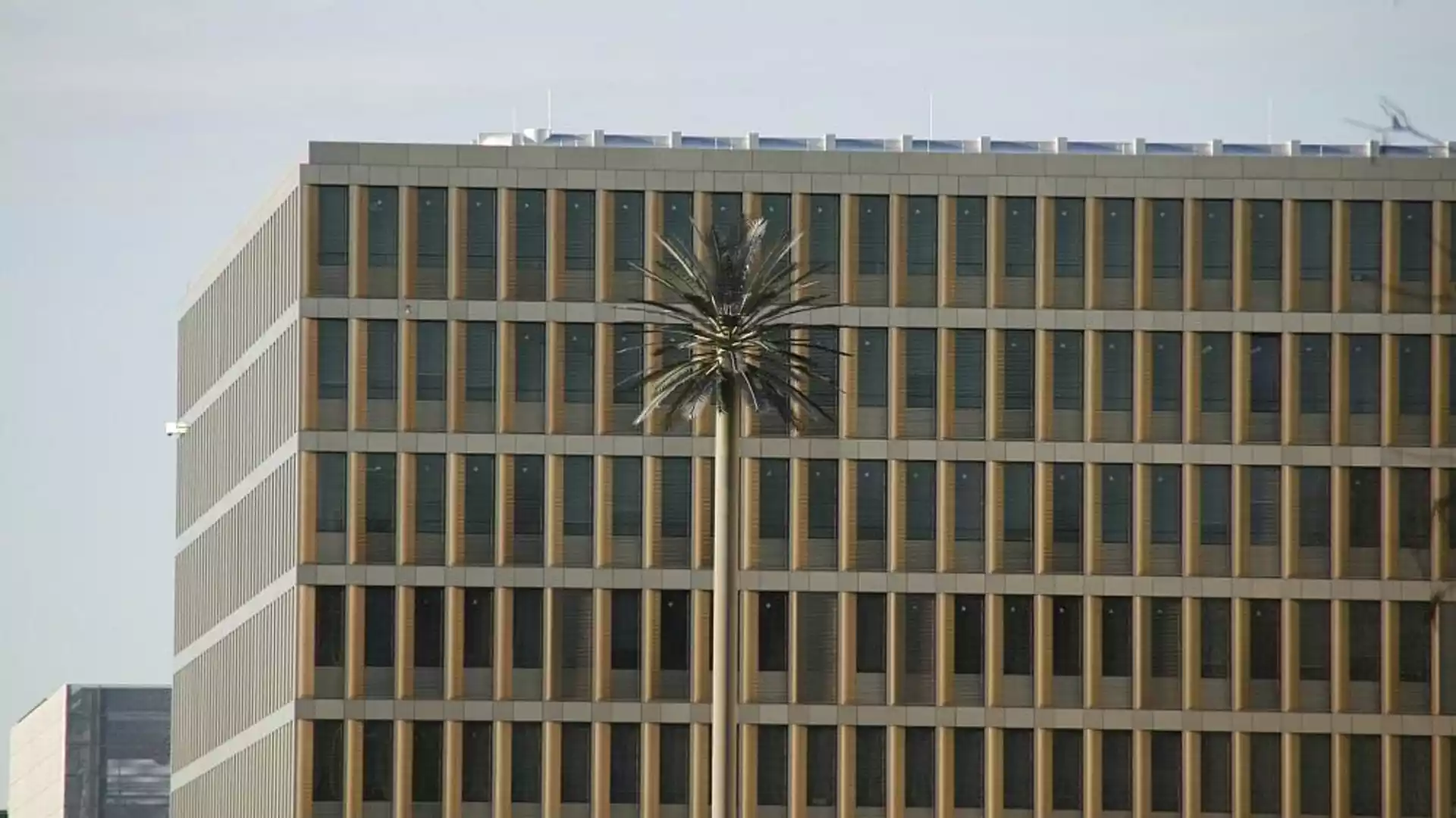 Außenansicht eines modernen Bürogebäudes mit vielen schmalen Fenstern und einer hohen Mastskulptur vor der Fassade.