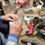 Ein Mann repariert an einem Arbeitstisch ein elektronisches Gerät mit Werkzeugen und Kabeln.