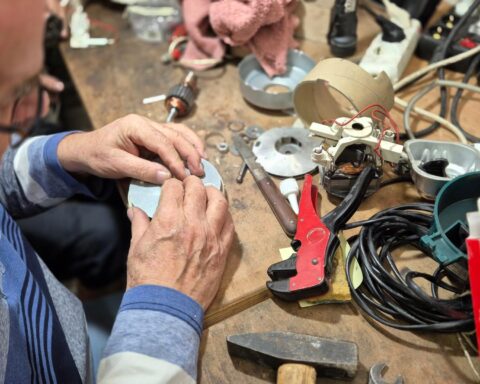 Ein Mann repariert an einem Arbeitstisch ein elektronisches Gerät mit Werkzeugen und Kabeln.
